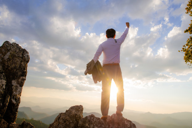 概念愿景，年轻的商人穿着舒适的休闲西装外套，手持商务包站在山顶，展望成功、竞争和领导者的理念。图片下载