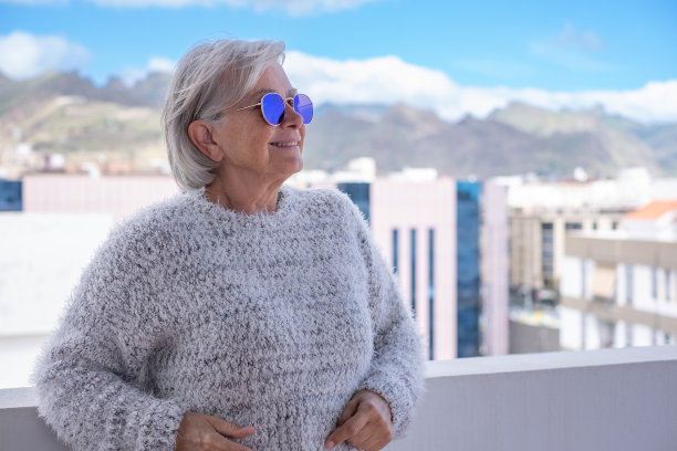 老年妇女微笑着看着城市风景的肖像。一个在户外戴着蓝色反光太阳镜的快乐老年妇女的脸。白发苍苍的退休女人图片下载