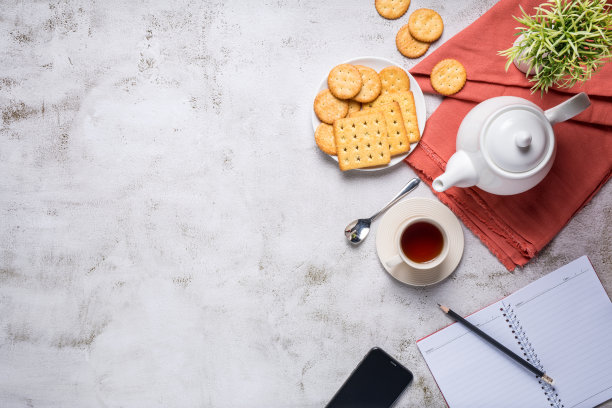 下午茶具上有面包、饼干、甜甜圈，旁边有手机和笔记本，有复印空间，俯视图。图片下载
