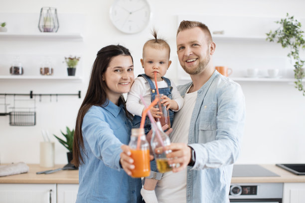 幸福的一家人捧着新鲜的果汁，在家里微笑图片下载