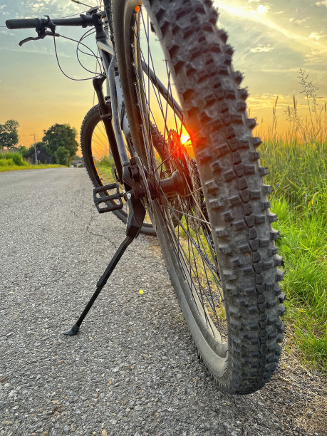 黑色山地自行车在乡村道路上，站在旁边的草地在日落，后视图图片下载