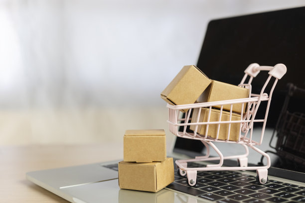 电脑笔记本电脑上的小购物车里的纸盒。超市送货上门服务。进出口，金融贸易。图片下载