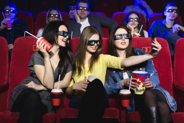 三个漂亮的女性朋友在电影院看电影时开心地笑着自拍图片下载