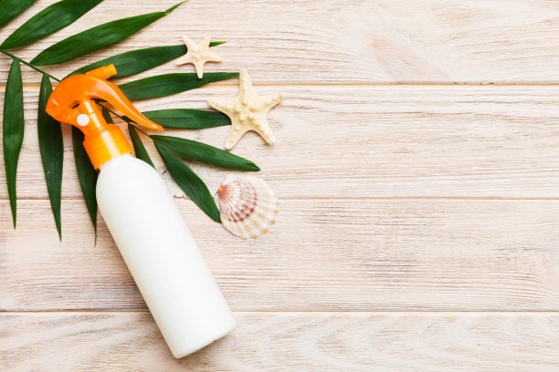 防晒喷雾瓶。瓶子与防晒霜和海洋贝壳与热带绿叶在彩色背景，俯视图图片下载