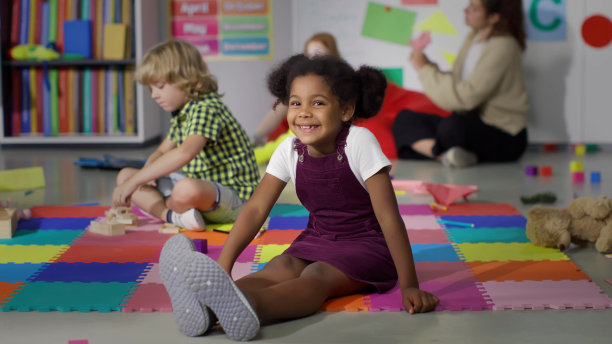 可爱的非裔美国女孩坐在地板上，对着镜头微笑图片下载