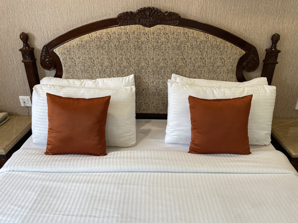 全画幅图片:白色酒店枕头叠在织物床头板上，白色羽绒被床罩，青铜色靠垫，重点放在前景图片下载