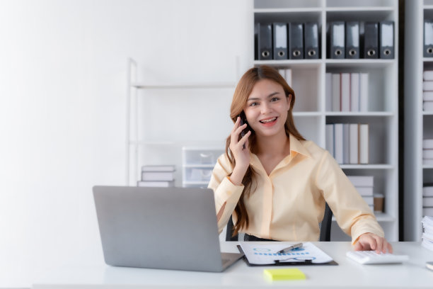 快乐美丽微笑的女商人在办公室用笔记本电脑打电话。图片下载