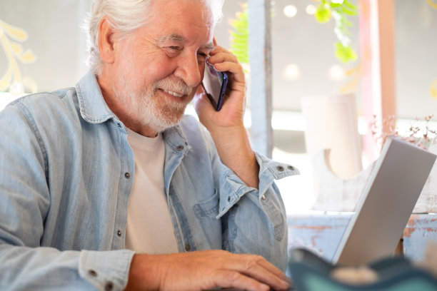 聪明的工作理念。咖啡店里微笑的老人一边用笔记本电脑一边打电话。老年人享受自由的生活方式，在遥远的地方工作图片下载
