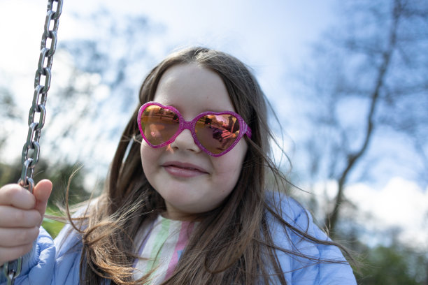 戴粉红色眼镜的年轻女孩在秋千上图片下载