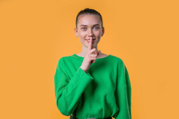 微笑的漂亮女人，手指放在嘴唇上——嘘，秘密，沉默，黄色画室图片下载