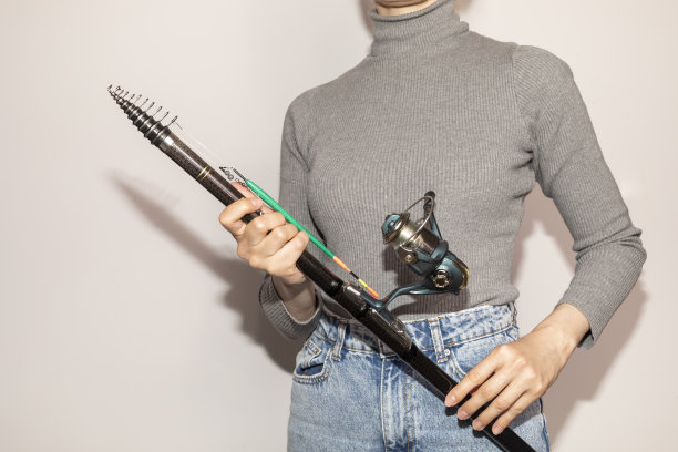 选择性聚焦裁剪女人持有钓鱼纺线杆，卷轴在白色背景。爱好、休闲、体育活动。水平面图片下载