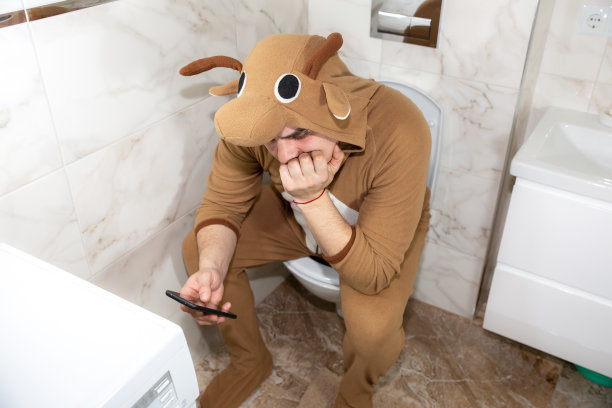 穿着奶牛角色扮演服装的男人。一个穿着滑稽动物睡衣的家伙坐在马桶上玩手机游戏。图片下载