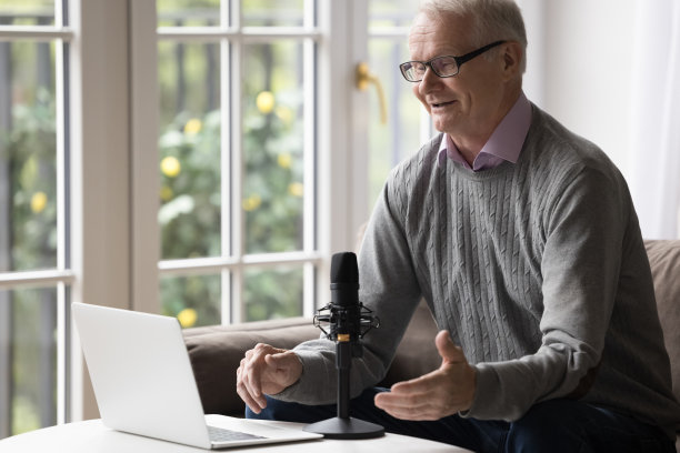 积极的退休老人对着麦克风和笔记本电脑摄像头讲话图片下载