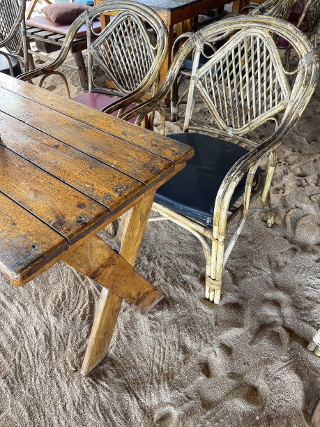 在天篷下的海滩餐厅用餐区，金色沙滩上的木制野餐餐桌，一组柳条扶手椅的特写图像，印度果阿的Palolem海滩，重点在前景图片下载