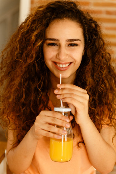 年轻漂亮的女人坐在厨房里喝着鲜榨橙汁图片下载