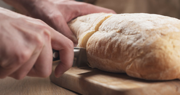 年轻人用手在砧板上切意大利面包图片下载