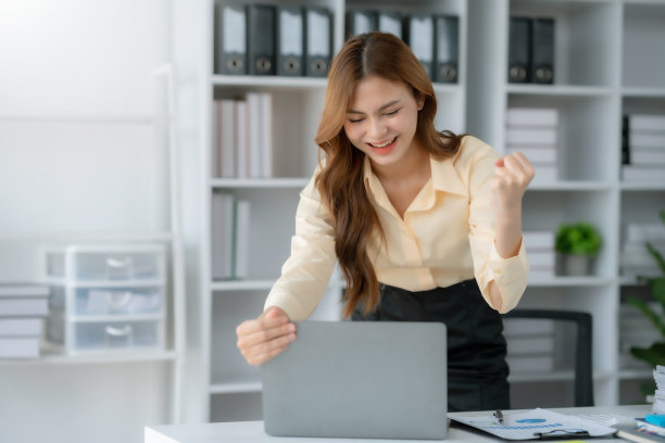 快乐的女商人举起胜利的手，拿着笔记本电脑开心地微笑。工作中成功的概念。图片下载