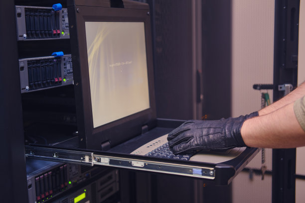 一名戴着黑色手套的男子正在安全服务器机房的终端键盘上打字。在服务器室工作时必须戴上手套，防止对硬件设备造成污染。图片下载