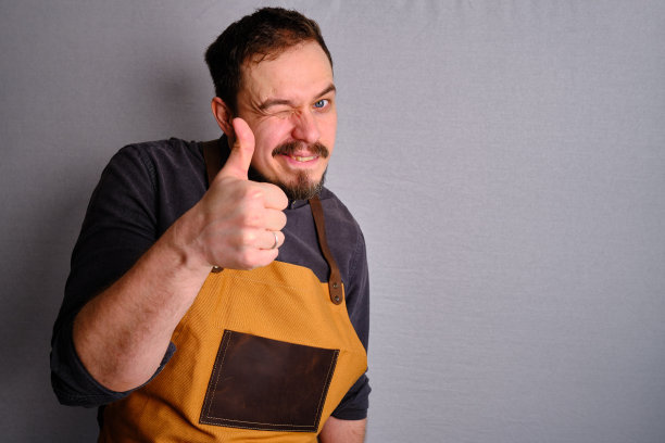 一个穿着厨房围裙的男人。厨师从事烹饪工作。穿着制服和防护服。食品服务方面的工作。专业烹饪。绿色面料围裙，休闲时尚服装。英俊的面包师摆姿势图片下载