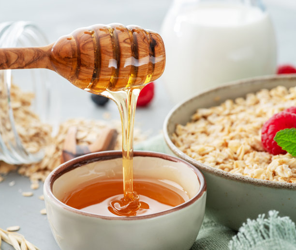 蜂蜜从木制的蜜壶里滴下来。背景是燕麦粥。图片下载