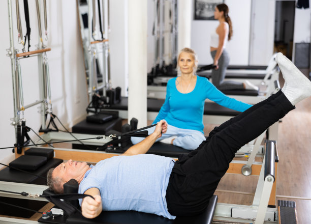 一名老人躺在康复中心的改造床上，专心地做腰部普拉提练习图片下载