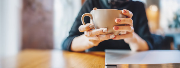 坐在咖啡桌旁的女人。她手里拿着一杯咖啡。图片下载