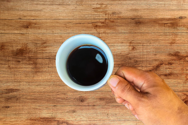 一个男人的手拿着一杯咖啡在木桌子上图片下载