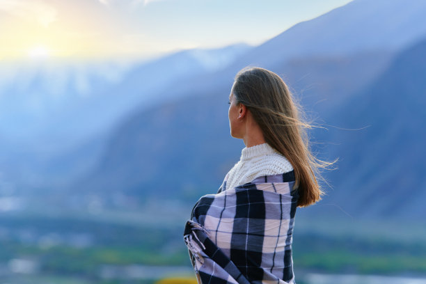 一个安静平和的女人裹着一条毯子，独自站在那里沉思，望向远方。女性享受自由和平静图片下载