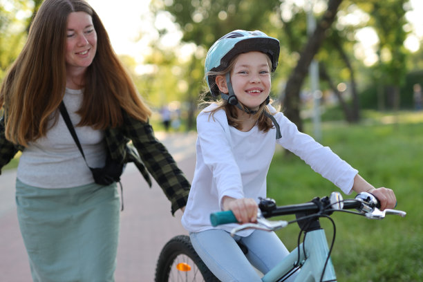 妈妈推着女孩骑自行车，教她骑车。图片下载