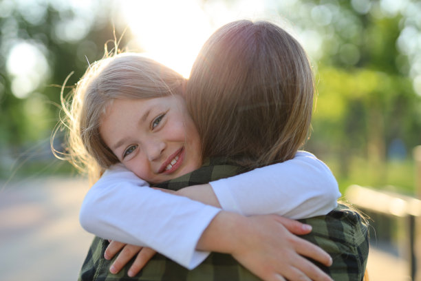 一个可爱的女孩在公园的夕阳下拥抱她的妈妈。图片下载