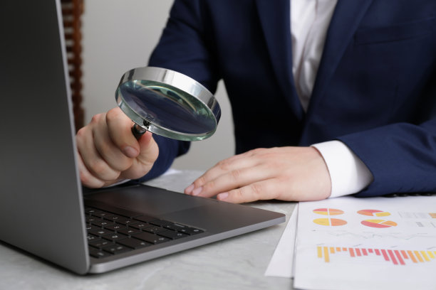 一个人在浅灰色的桌子上拿着放大镜靠近笔记本电脑，特写。在线搜索概念图片下载