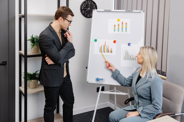 自信的商业教练在活动挂图上做演示。一个年轻的女人和一个男人正在办公室里谈论商业项目的时间表图片下载