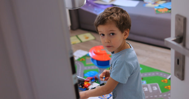 打开门进入男孩房间，看到孩子在玩玩具。惊讶的孩子看着一个悄悄闯入房间的人。图片下载