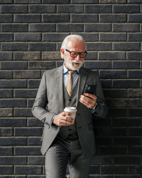 一位资深商人站在户外，手里拿着智能手机和咖啡图片下载