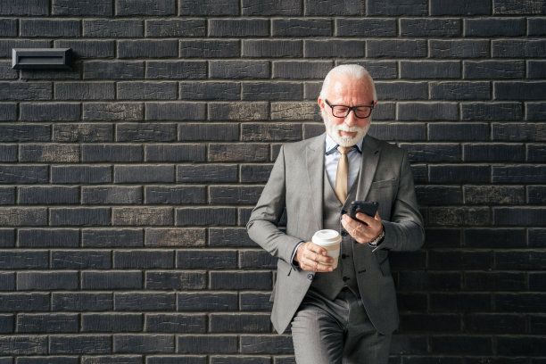 一位资深商人站在户外，手里拿着智能手机和咖啡图片下载