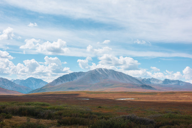 五彩缤纷的秋景，阳光明媚的高山高原，湖泊和美丽的山顶下戏剧性的多云的天空。鲜艳的秋色笼罩着群山。多变天气中的云影。图片下载