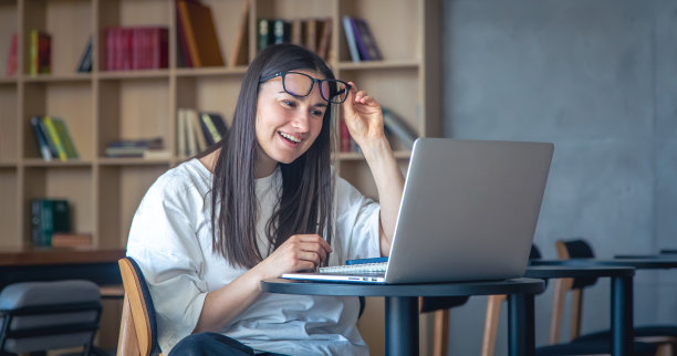 戴着眼镜坐在笔记本电脑前的开朗的年轻女子。图片下载