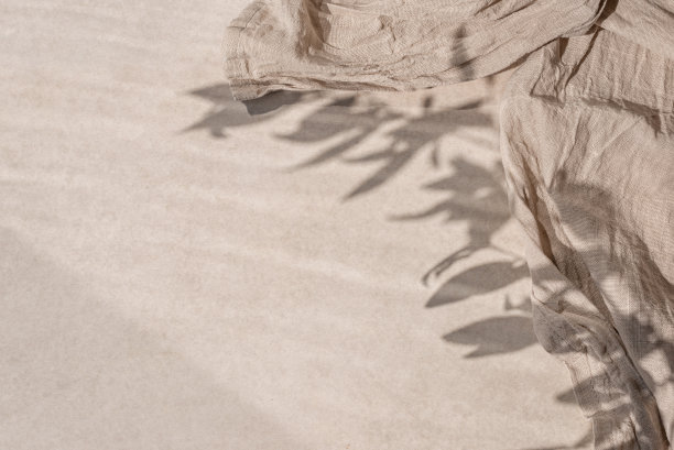 中性米色陶瓷石材桌面纹理背景与皱巴巴的亚麻织物和美学花卉阳光阴影。极简的商业品牌模板，框架与复制空间图片下载