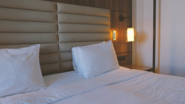 在现代室内设计的家庭或酒店中，卧室的特写片段与空的床头柜，打开阅读灯和插座。柔软的枕头和毯子，时尚舒适的家具。图片下载