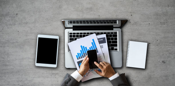 商业工作者的手拿着智能手机，平板电脑和笔记本电脑在现代办公桌上，办公用品俯视图。图片下载