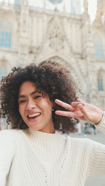 年轻女子正坐在手机前。一个女孩举着胜利的手势，在老城的背景下自拍图片下载
