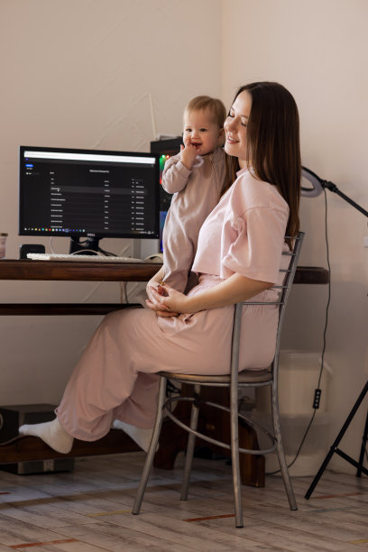 一位怀抱婴儿的年轻母亲远程在家用电脑工作图片下载