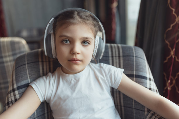5岁蓝眼睛女婴的肖像，戴着耳机坐在椅子上听音乐图片下载