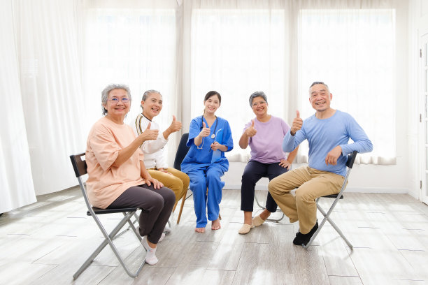 在老年人群体治疗中，护理治疗师与一群亚洲老年人坐在一起，竖起大拇指围成一个圈，检查他们的身心健康状况。养老院为图片下载