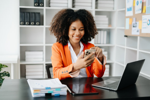 年轻的非洲妇女坐在黑色办公桌旁，用平板电脑和笔记本电脑打字图片下载