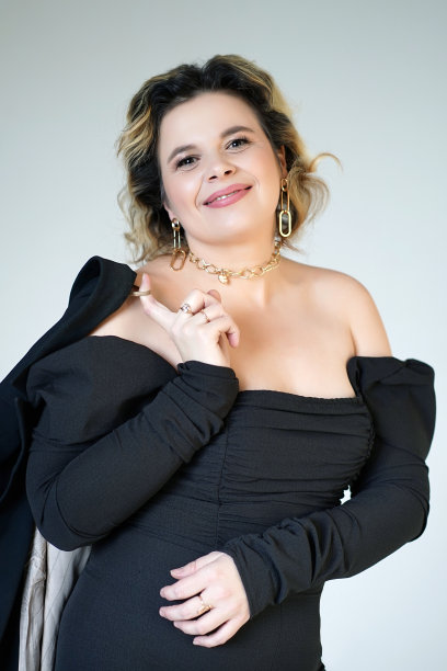 一位身穿黑色西装、面带微笑的女子站在那里，肩上披着一件白色背景的夹克。图片下载