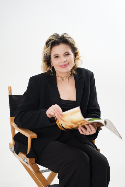 一位身穿黑色西装、面带微笑的女士拿着一本杂志坐在椅子上。图片下载