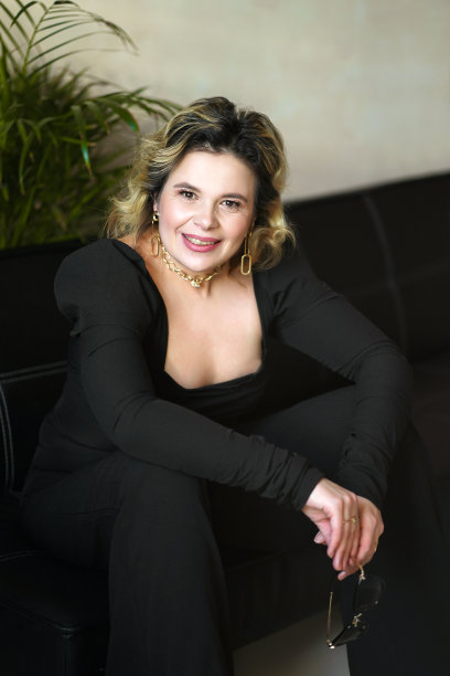 一位身穿黑色西装、面带微笑的女士拿着眼镜坐在那里。图片下载