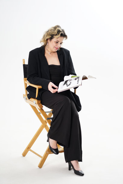 一位身穿黑色西装、面带微笑的女士拿着一本杂志坐在椅子上。图片下载