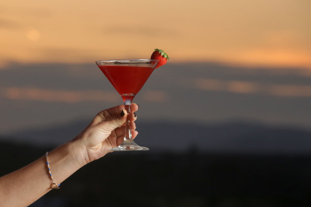 女子端着一杯草莓代基里鸡尾酒，身后是美丽的夕阳图片下载